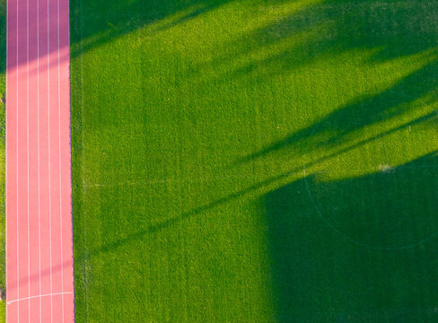 Aerial view of the Sports and Recreation Center featuring a green grass pitch and red running track with long shadows in Starogard Gdanski, Pomeranian Voivodeship, Poland.