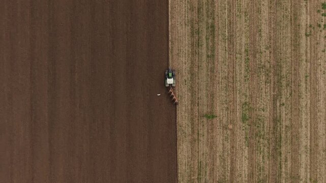 Tractor Plowing Field: An aerial view captures a tractor cultivating a split field, with one side freshly plowed and the other showing remnants of the previous harvest.