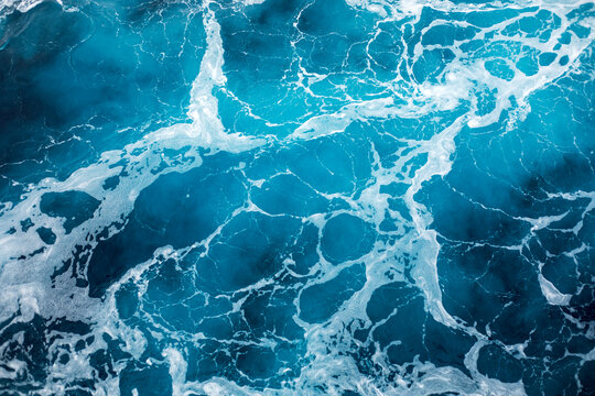 Blue ocean surface with gentle ripples and sparkling sunlight reflections, creating a calm, serene natural background with beautiful water texture.