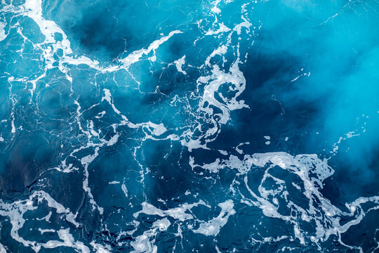 Blue ocean surface with gentle ripples and sparkling sunlight reflections, creating a calm, serene natural background with beautiful water texture.