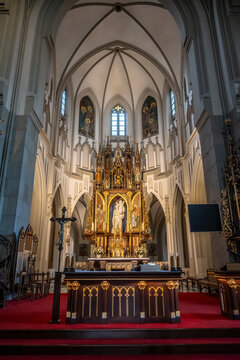 The lavish main altar, featuring a magnificent gilded altarpiece, crucifix, and red carpet, stands beneath soaring vaulted ceilings in Krakow, Poland.