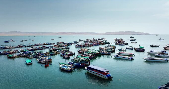 Aerial view of colorful fishing boats moored in turquoise harbor waters near desert coastline.