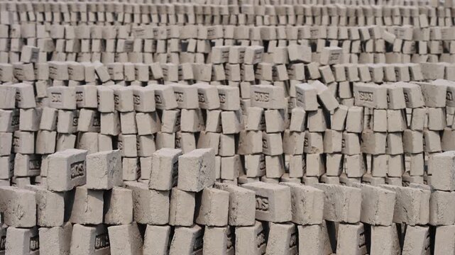 Rows of grey concrete bricks drying under sun at construction material site.