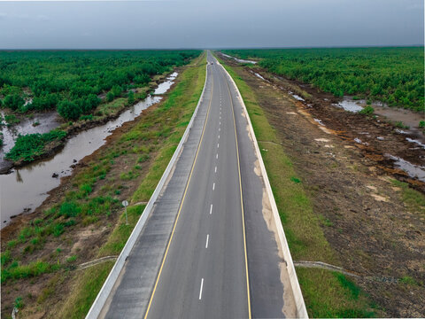 Aerial view of a long asphalt road stretching through the lush mangrove forests and wetlands of Bonny Island, Bonny Town, Rivers, Nigeria.