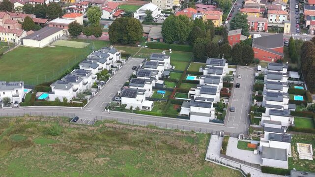 Modern Housing Development: An aerial view showcases a contemporary housing development with rows of sleek, modern homes featuring solar panels and private swimming pools, nestled beside green spaces.