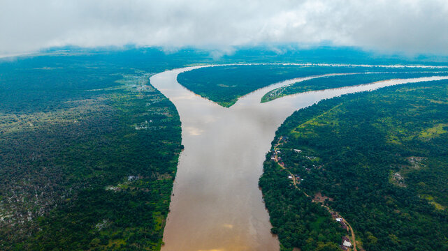 Aerial view of the confluence of the Cross River and Calabar River surrounded by lush tropical rainforest under a cloudy sky in Itu, Akwa Ibom, Nigeria.