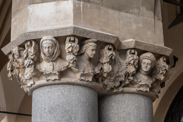 Intricately detailed Renaissance stone column capitals display sculpted human faces and elegant foliage motifs on Sukiennice Cloth Hall in the Main Market Square in Krakow, Poland. © Danica Chang