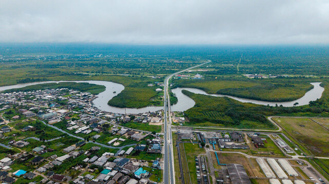 Aerial view of the winding Kwa Ibo River flowing through lush green mangroves and residential areas with a long bridge crossing the water in Kwa Ibo, Akwa Ibom, Nigeria.