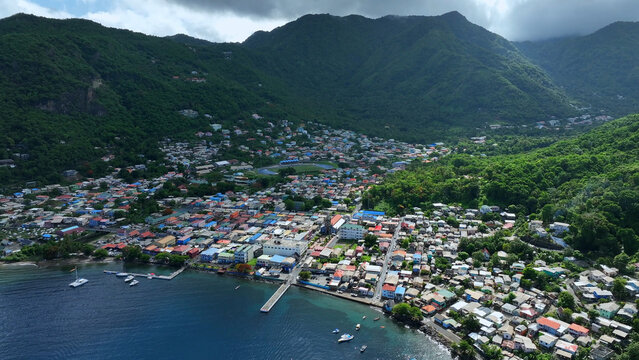 Aerial view of the coastal town of Soufriere nestled between lush green mountains and the Caribbean Sea, featuring colorful buildings, a pier, and boats in Soufriere, Soufriere, Saint Lucia.