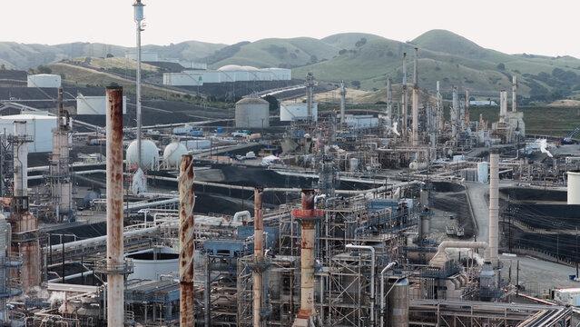 Aerial view of the oil refinery in Rodeo featuring industrial storage tanks, complex piping systems, and tall chimneys set against rolling hills in Rodeo, California, United States.