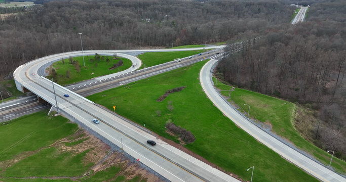 Aerial view of a highway interchange with looping ramps and surrounding green grassy fields and dense forest in Manheim, Pennsylvania, United States.