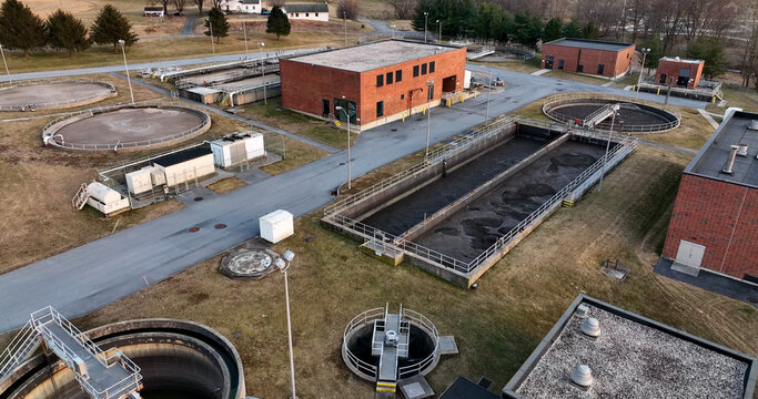 Aerial view of a wastewater treatment plant with circular sedimentation tanks and rectangular aeration basins surrounded by brick buildings and grassy grounds in Lititz, Pennsylvania, United States.