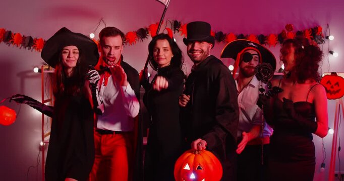 Happy young people group in carnival costumes scaring with hands and dancing together celebrating Halloween party at home. Friends having fun on holiday. Celebration concept. 4k video. Slow motion.