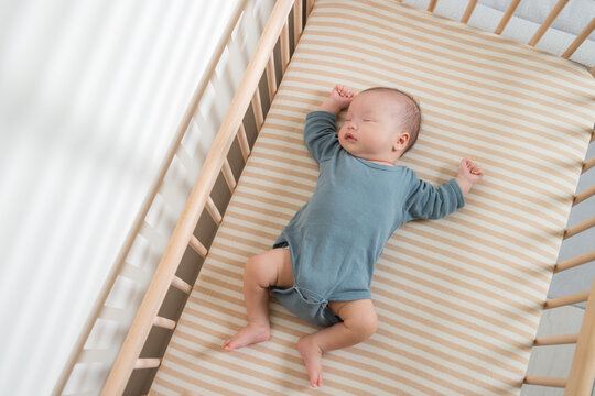Small baby sleeping peacefully inside a wooden crib on striped sheet