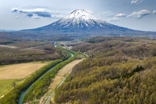 Aerial view of Mount Yotei with its snow-capped peak rising above the winding river, agricultural fields, and lush forests in Niseko, Hokkaido, Japan.