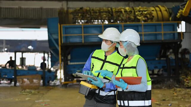 Midsection of two industrial workers in safety vests using a digital tablet to inspect organic waste processing