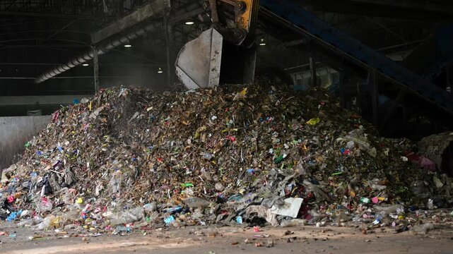 Heavy machinery dumps huge piles of mixed trash in an industrial recycling center. A stark look at waste management, pollution, and the need for global sustainability.