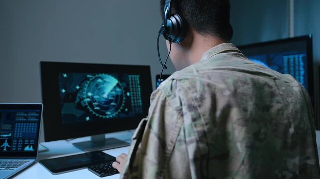 Asian male military officer in camouflage uses a tablet and monitors radar screens in a high-tech command center, focusing on national defense