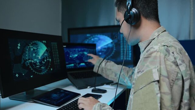 Asian male military officer in camouflage uses a tablet and monitors radar screens in a high-tech command center, focusing on national defense