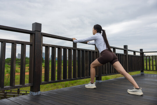 Asian woman performing side lunge stretch holding wooden railing outdoors