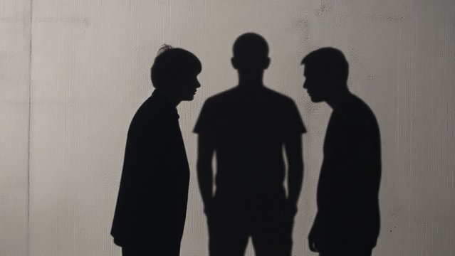 Silhouette of Three People Engaged in Conversation Against Wall