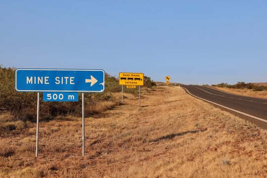 Blue road sign indicating a mine site entrance ahead with a warning notice for road train vehicles entering the highway in the Australian outback with copy space for text