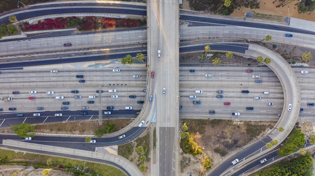 Aerial view of a complex highway interchange with multiple lanes of traffic and a curved ramp surrounded by palm trees and urban landscaping in Los Angeles, California, United States.
