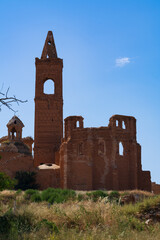 An ancient ruined bell tower rises above collapsed walls of a deserted settlement in dry grassland. Ornate brickwork and pointed arches showcase the faded grandeur of this crumbling abandoned landmark © Aimur