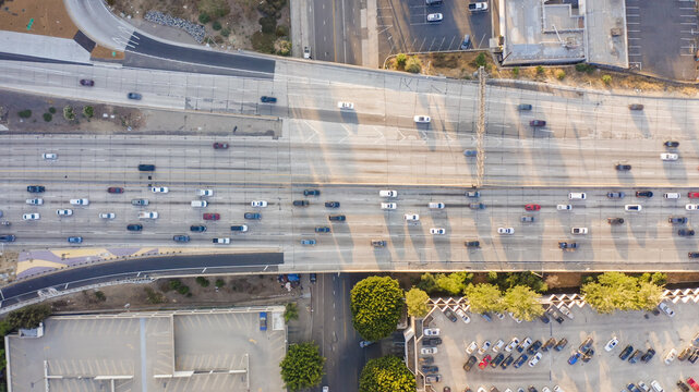 Aerial view of a busy freeway interchange with multiple lanes of traffic and adjacent parking lots in Los Angeles, California, United States.