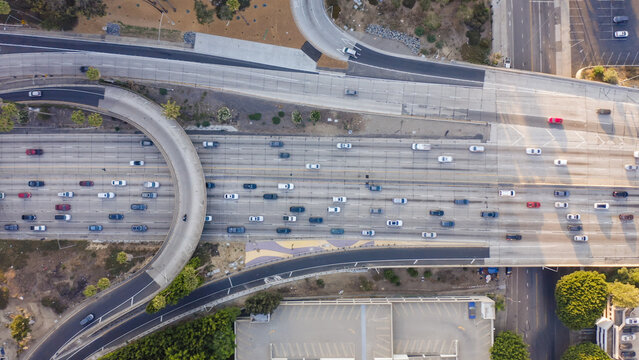 Aerial view of a busy highway interchange with multiple lanes of traffic, cars, concrete road surfaces, and surrounding greenery in Los Angeles, California, United States.