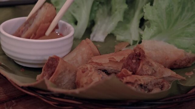 Detail shot close-up, chopsticks picking a piece of vietnamese fried springrolls (Cha Gio) soaking it in vinegar dipping sauce (Nuoc cham). Authentic local food of Vietnam