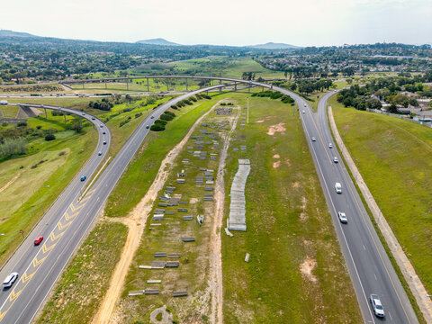 Aerial view of the highway interchange in Brackenfell with cars driving on asphalt roads, surrounded by grassy embankments and suburban landscape in Cape Town, Western Cape, South Africa.