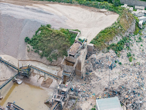 Aerial view of the Philippi industrial site with a dump truck unloading material into a conveyor system surrounded by piles of sand and gravel in Cape Town, Western Cape, South Africa.