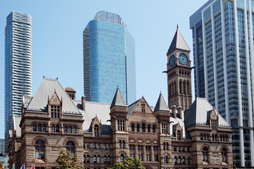Obraz premium Historic Old City Hall clock tower framed by modern skyscrapers in downtown Toronto on a bright clear day. g.