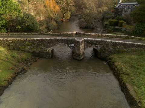 Aerial view of the historic stone bridge spanning the River Lerryn, surrounded by lush trees and greenery in the countryside of Lerryn, Cornwall, United Kingdom.