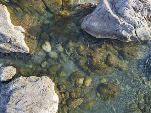Aerial view of the clear, shallow waters of the Kiri River flowing over smooth river stones and large boulders in Shkoder, Qarku i Shkodres, Albania.