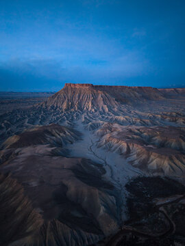 Aerial view of the rugged badlands and eroded rock formations of the desert landscape under a deep blue twilight sky in Caineville, Utah, United States.
