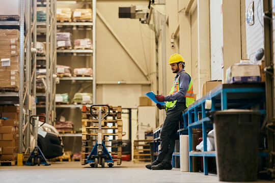 Logistic manager analyzing inventory list while working in industrial warehouse.