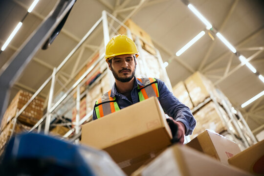 Below view of worker stacking cardboard boxes in distribution warehouse.