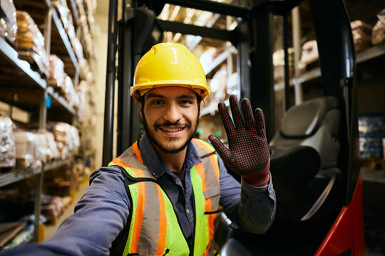 Happy forklift operator taking selfie in distribution warehouse and looking at camera.
