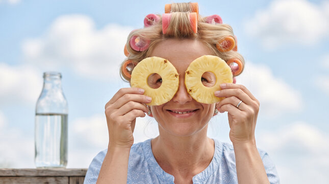 Woman with hair curlers holding pineapple rings over eyes outdoors