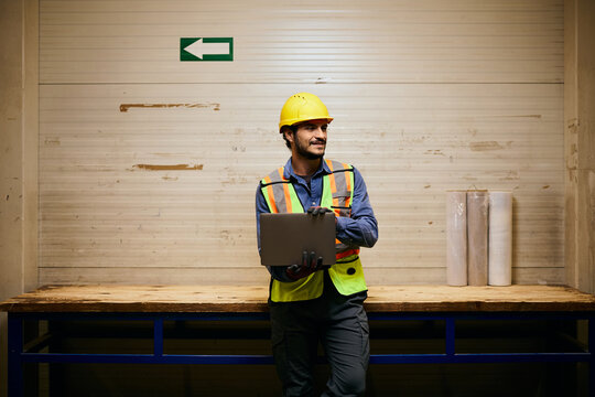 Happy industrial warehouse worker working on laptop.