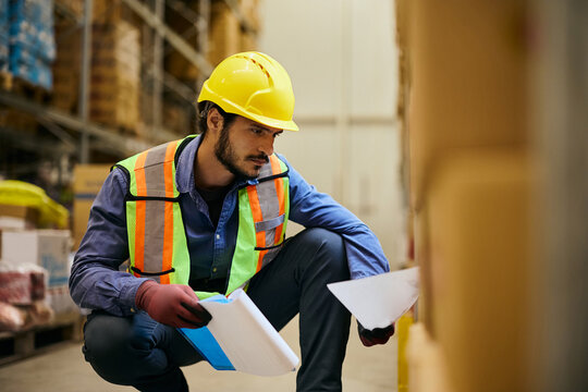 Logistics worker checking shipment labels on boxes in distribution warehouse.