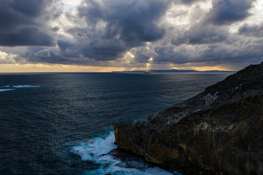 Aerial view of Sharp Point Lookout with dramatic storm clouds over the Southern Ocean, sunbeams, rugged coastal cliffs, and crashing waves in Torndirrup, Western Australia, Australia.