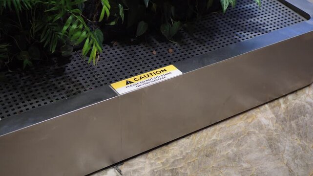 Close up on planter box with caution sign, demonstrating a subtle shift and environmental detail.