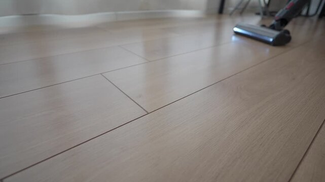 Close up shot of cordless vacuum cleaner cleaning wooden floor motion