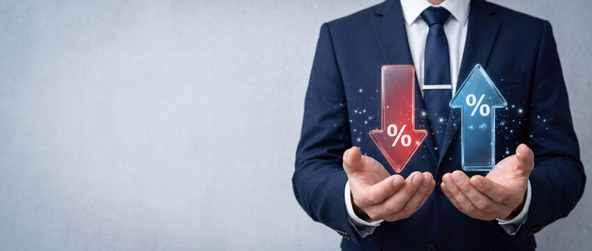 Businessman in formal suit holding glowing digital red down arrow and blue up arrow with percentage symbols, representing interest rates, financial market fluctuations, and economic trends.