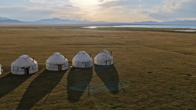 Aerial view of traditional yurts set in the vast landscape of Song-Kul at golden hour with mountains in the background in Naryn Region, Kyrgyzstan.
