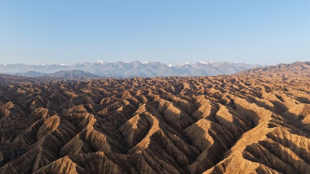 Aerial view of the rugged, eroded sandstone formations of the Skazka Canyon landscape with snow-capped mountains in the distance in Issyk-Kul Region, Kyrgyzstan.