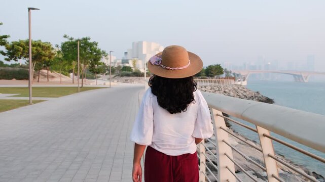 Tourist woman strolling on Saadiyat waterfront promenade with Natural History Museum Abu Dhabi visible in cultural district background